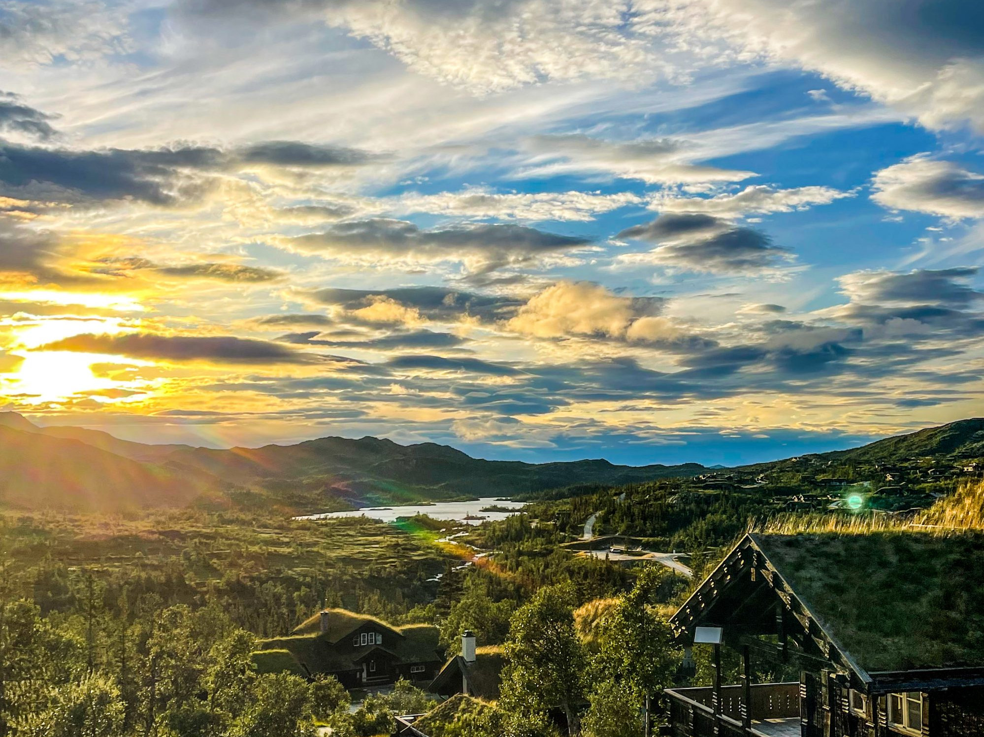 Sunset over scenic landscape with grass-roofed cabin, capturing 