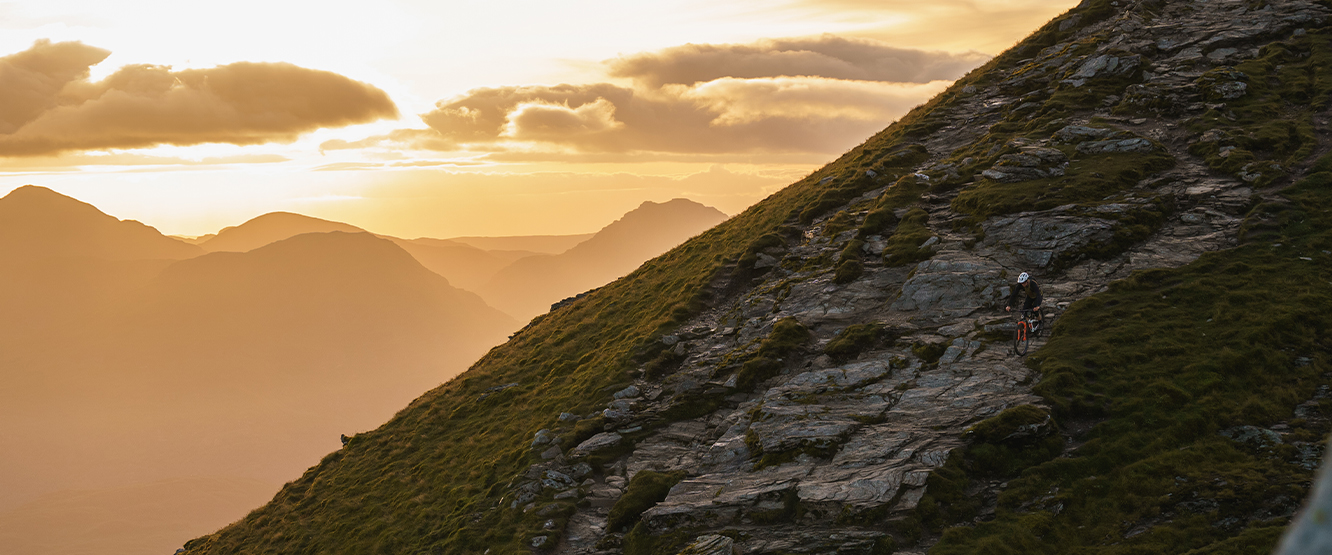Mountain biking at sunset on a rugged Scottish hillside, featured in Scotty's Scotland Showcase Season 2. Scenic adventure landscape. Mountain Bike United.