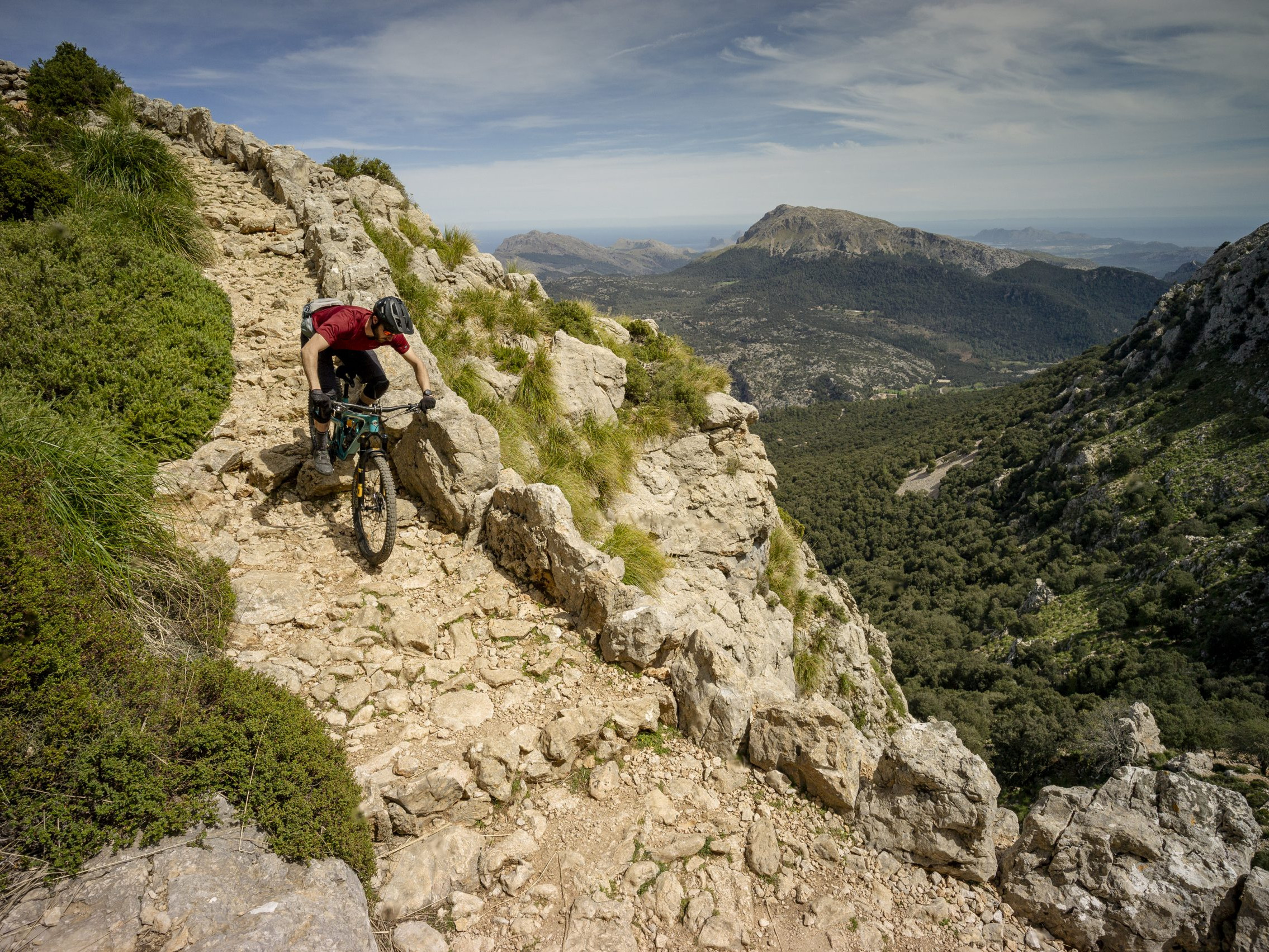 Mountain biker on rocky trail in scenic mountain landscape, wearing helmet and red shirt, cycling adventure, nature exploration, outdoor activity. Mountain Bike United.