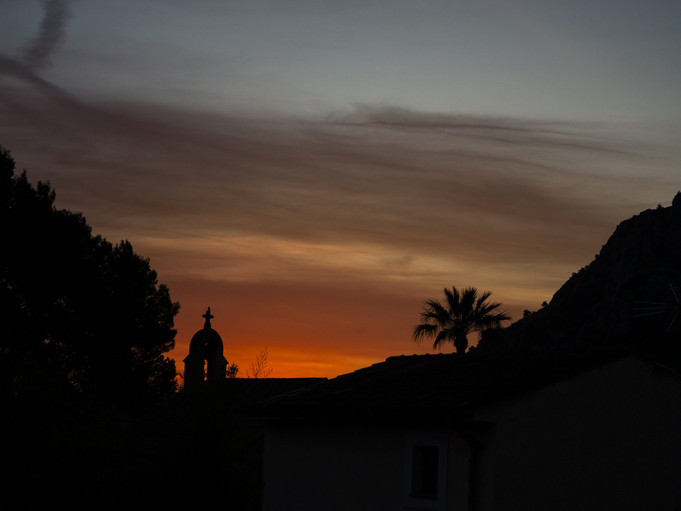 Sunset silhouette with church bell tower, palm tree, and hillside. Twilight sky with orange, purple hues creates a serene landscape view. Mountain Bike United.