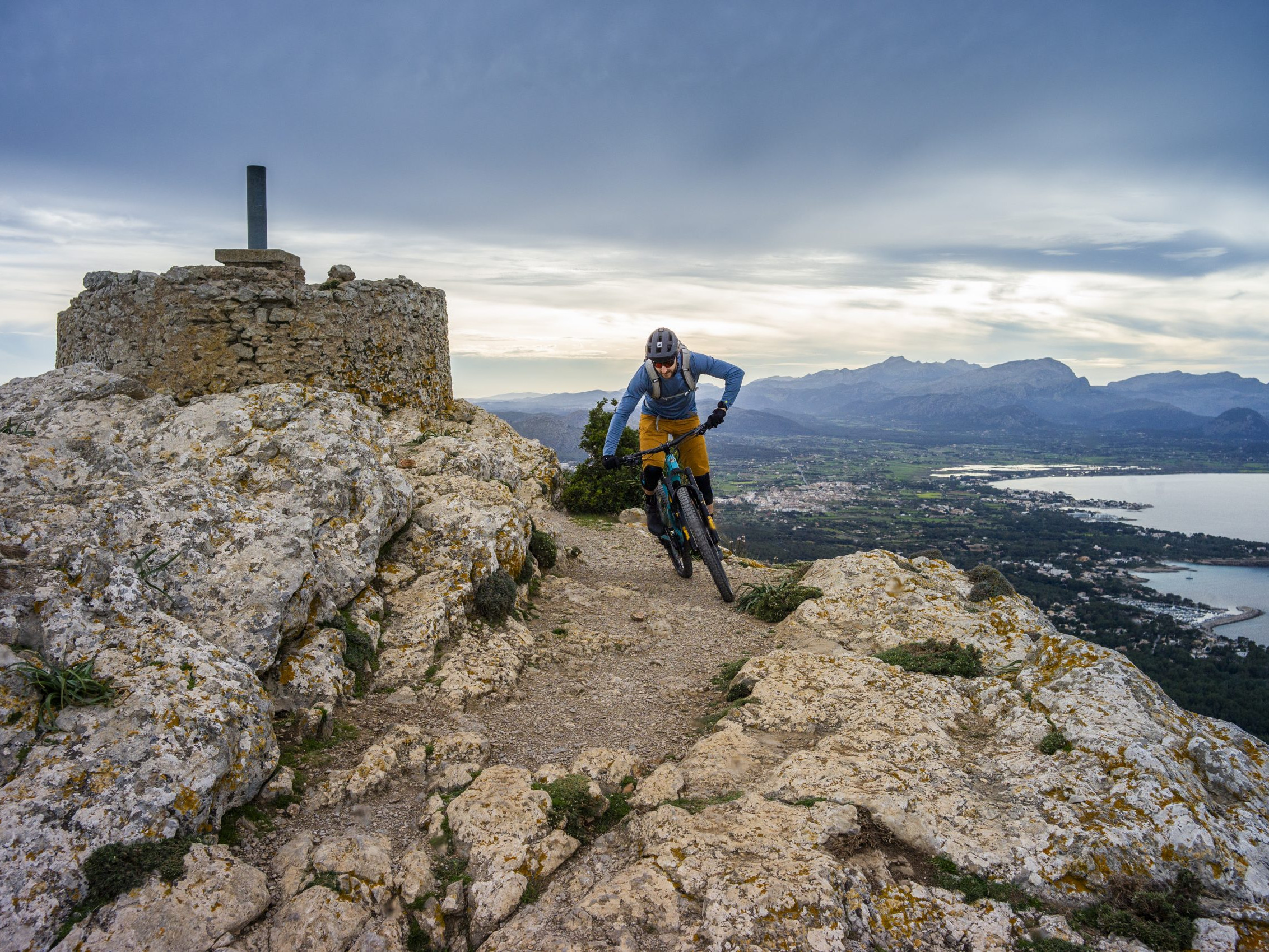 Mountain biker on rocky trail with scenic coastal view in the background, embracing adventure sports and outdoor biking experience on rugged terrain. Mountain Bike United.