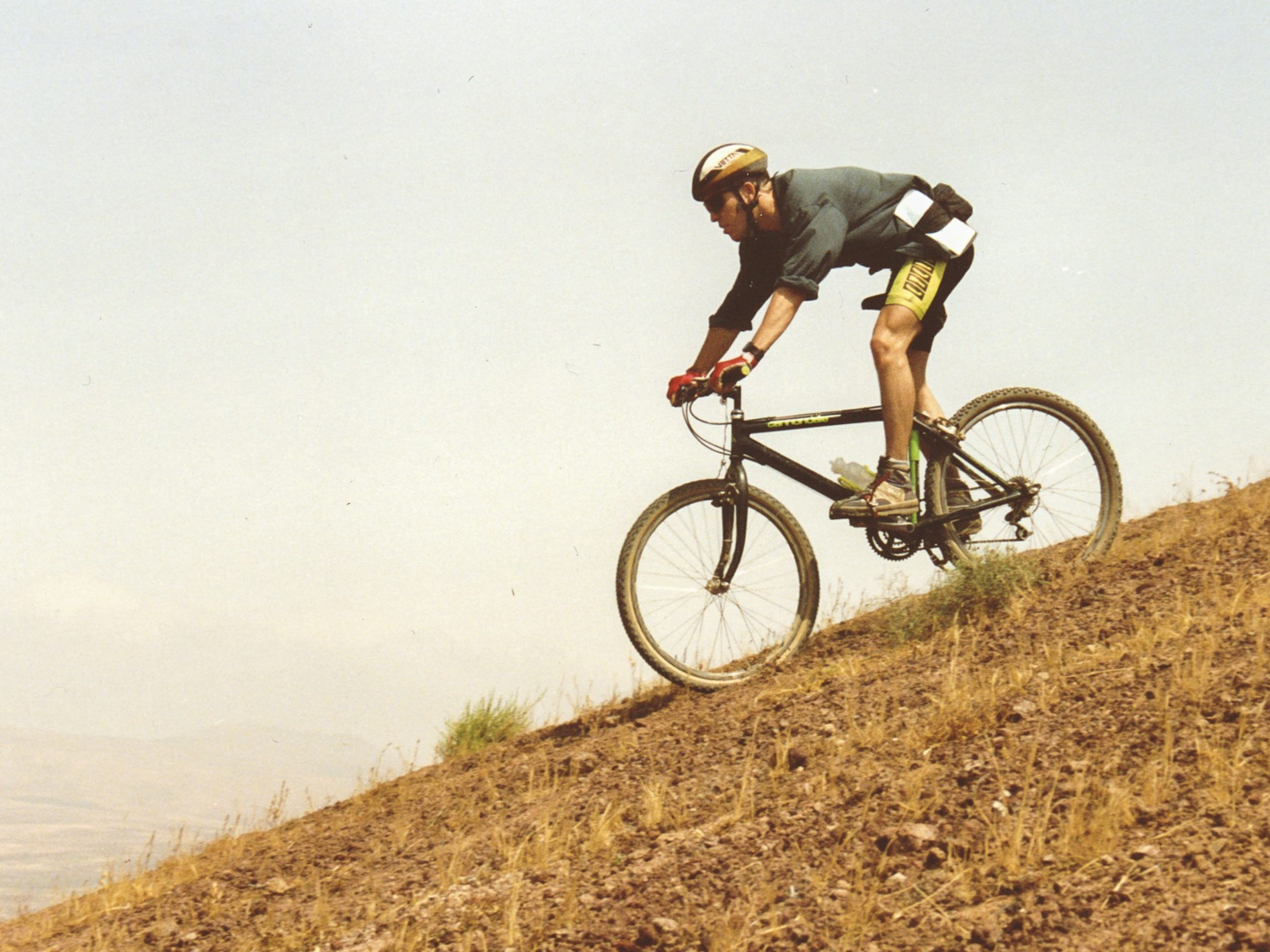 Mountain biker descends steep hillside wearing helmet and gloves, showcasing outdoor adventure and cycling skill. Mountain Bike United.