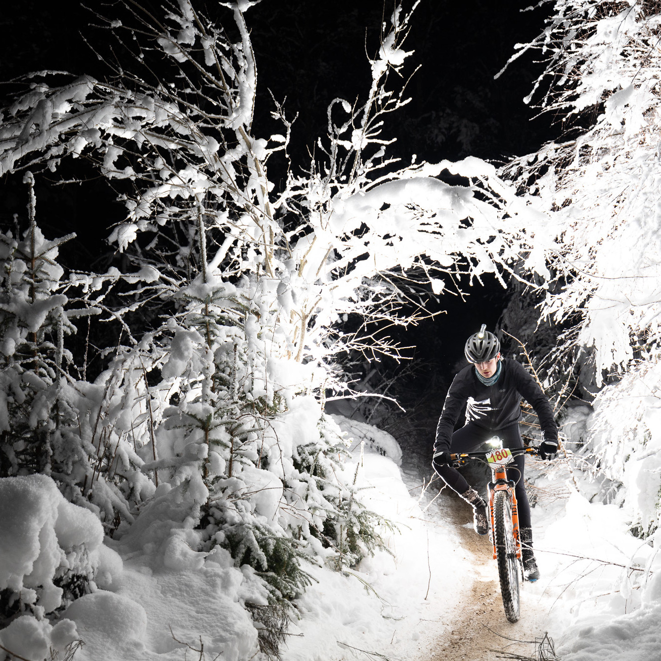Mountain biker rides through snowy forest trail at night, wearing protective gear. Winter cycling adventure, outdoor sports, night biking. Mountain Bike United.