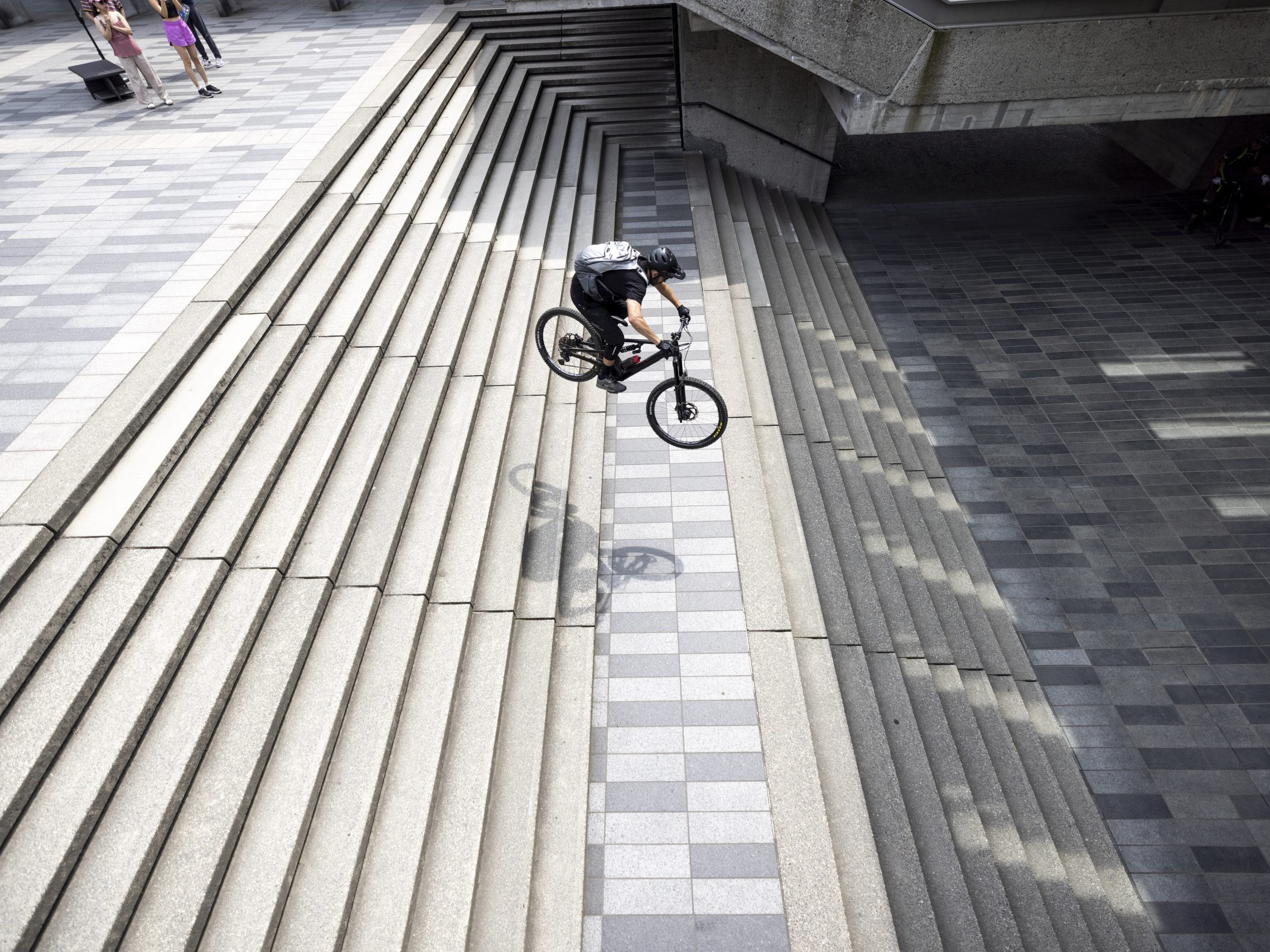 Urban cyclist performing a jump down concrete stairs, showcasing BMX skills. Search keywords: Hans Rey, mountain bike tricks, urban cycling. Mountain Bike United.