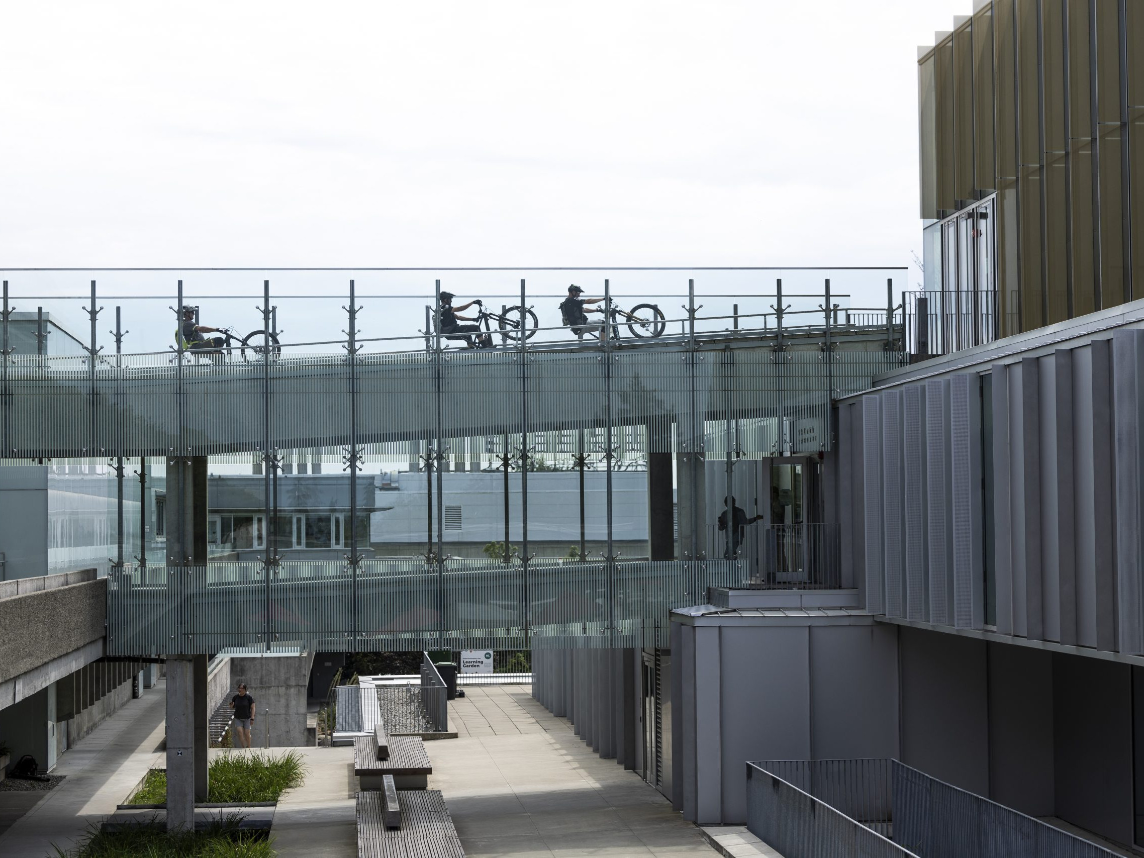 Hans Rey and bikers on a glass walkway outside a modern building, highlighting cycling architecture and urban design in an urban environment. Mountain Bike United.