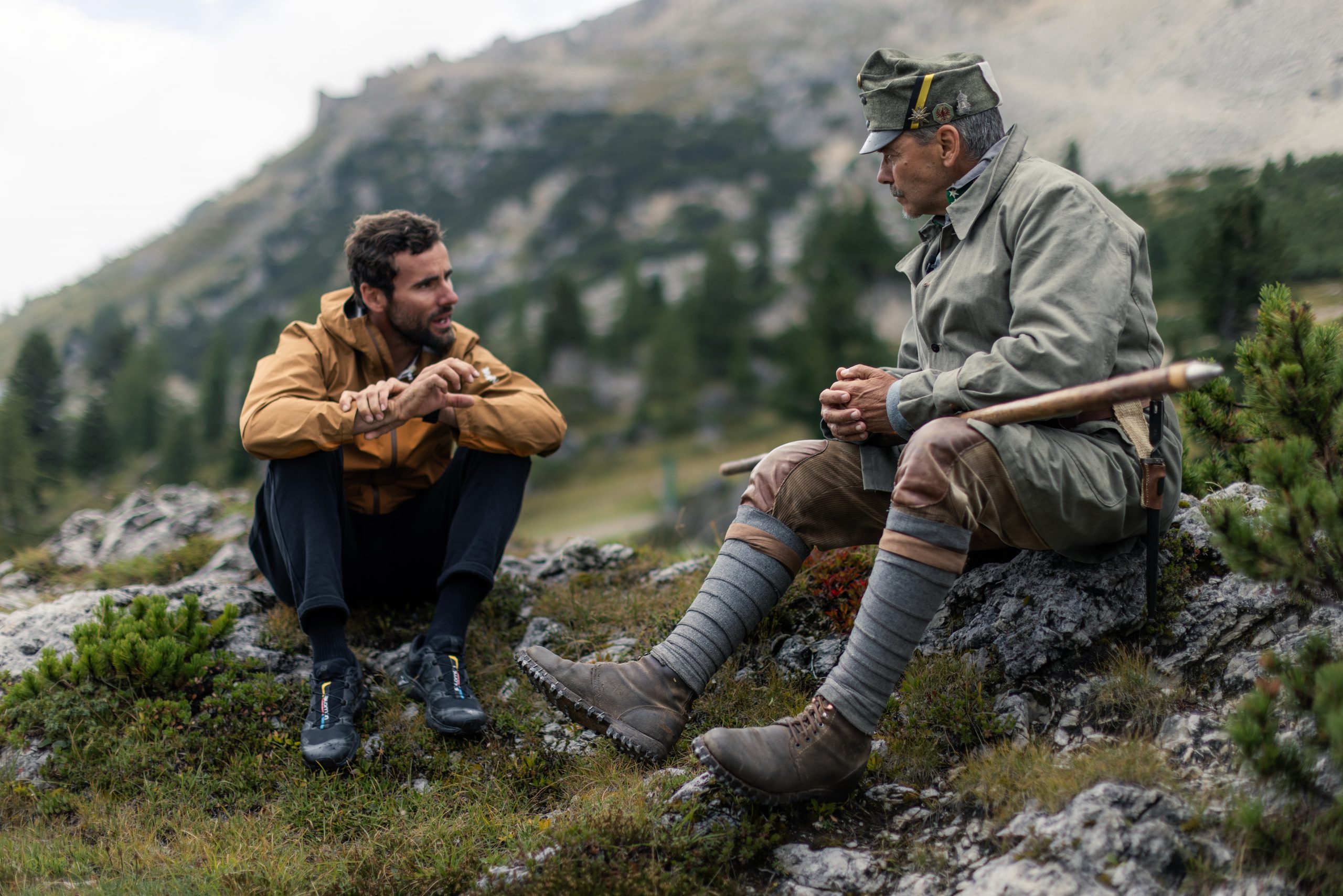 Kilian Bron conversing with a local in the Dolomites, surrounded by mountainous landscape, emphasizing adventure and nature exploration. Mountain Bike United.