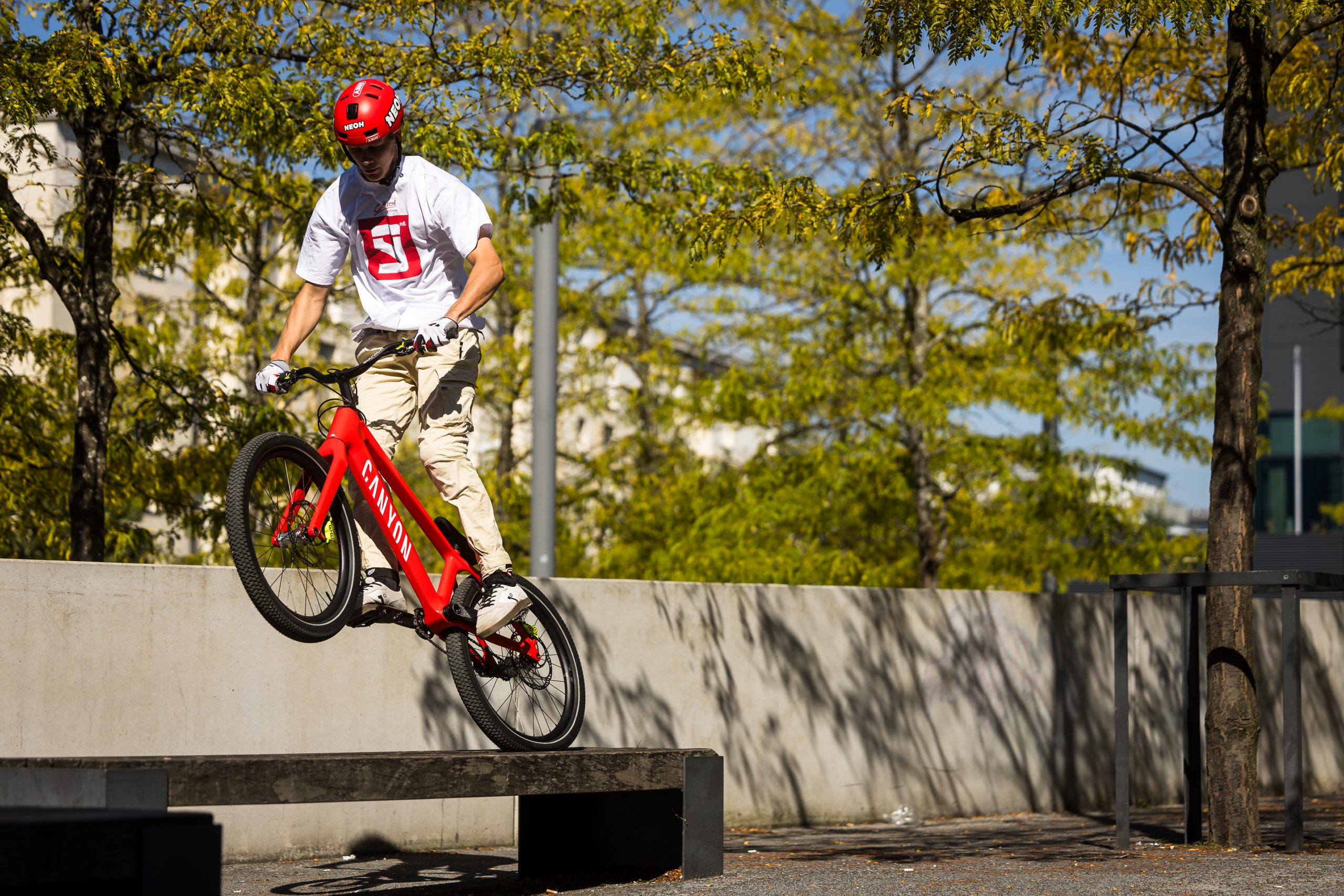 Gabriel Wibmer performing a bike trick on a red Canyon bike outdoors, showcasing his cycling skills in a park setting. Mountain Bike United.