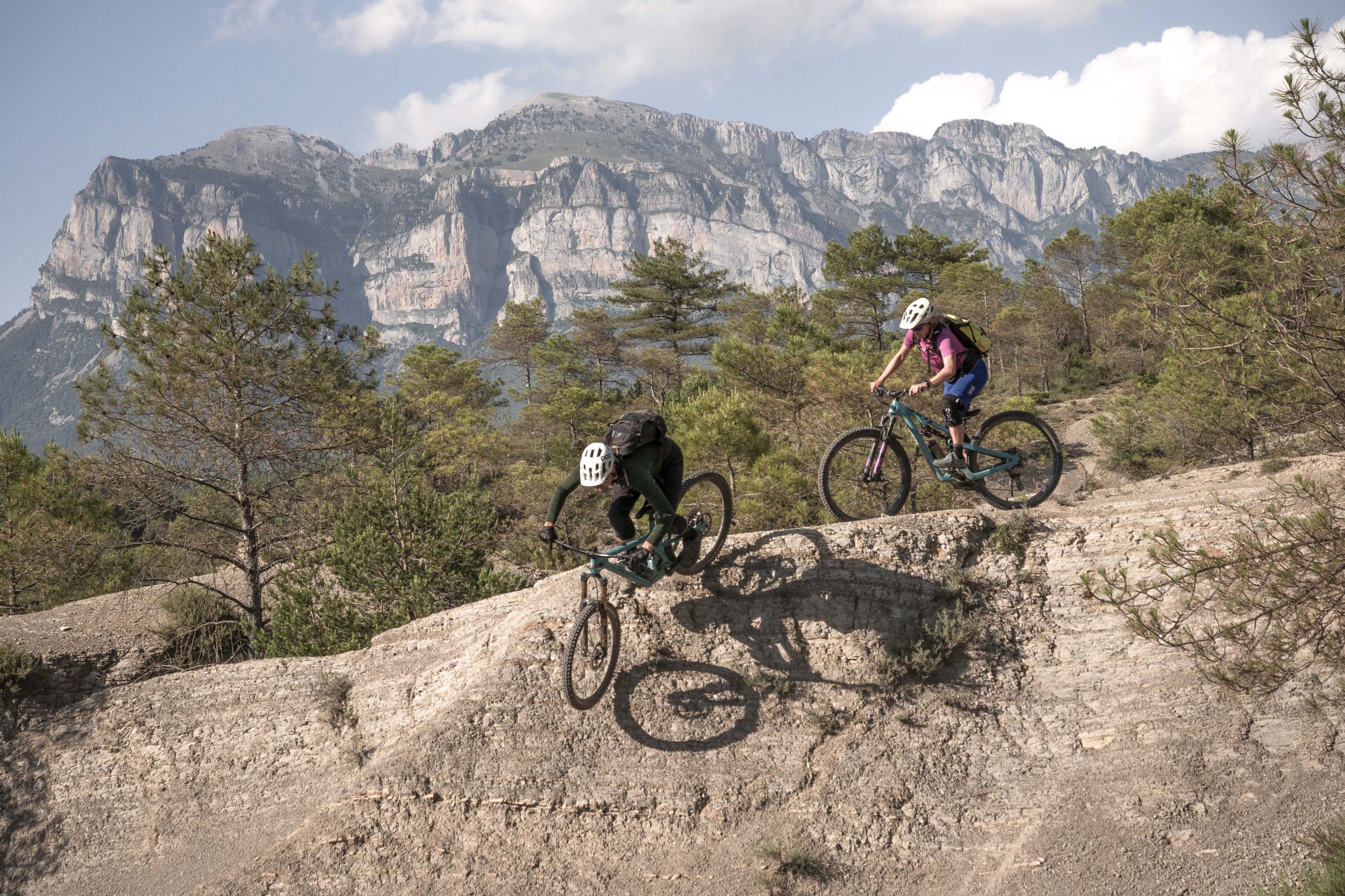 Mountain bikers on a trail in the Pyrenees, showcasing H+I Adventures experiences amid stunning cliffs and lush landscape. Mountain Bike United.